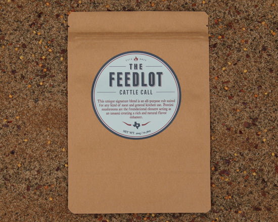 A brown paper package labeled "Cattle Call by The Feedlot" describes an all-purpose rub for grilling and smoking meat. Featuring porcini mushrooms as a natural flavour enhancer, it offers an umami and rich natural flavor. The package is set against a textured background.