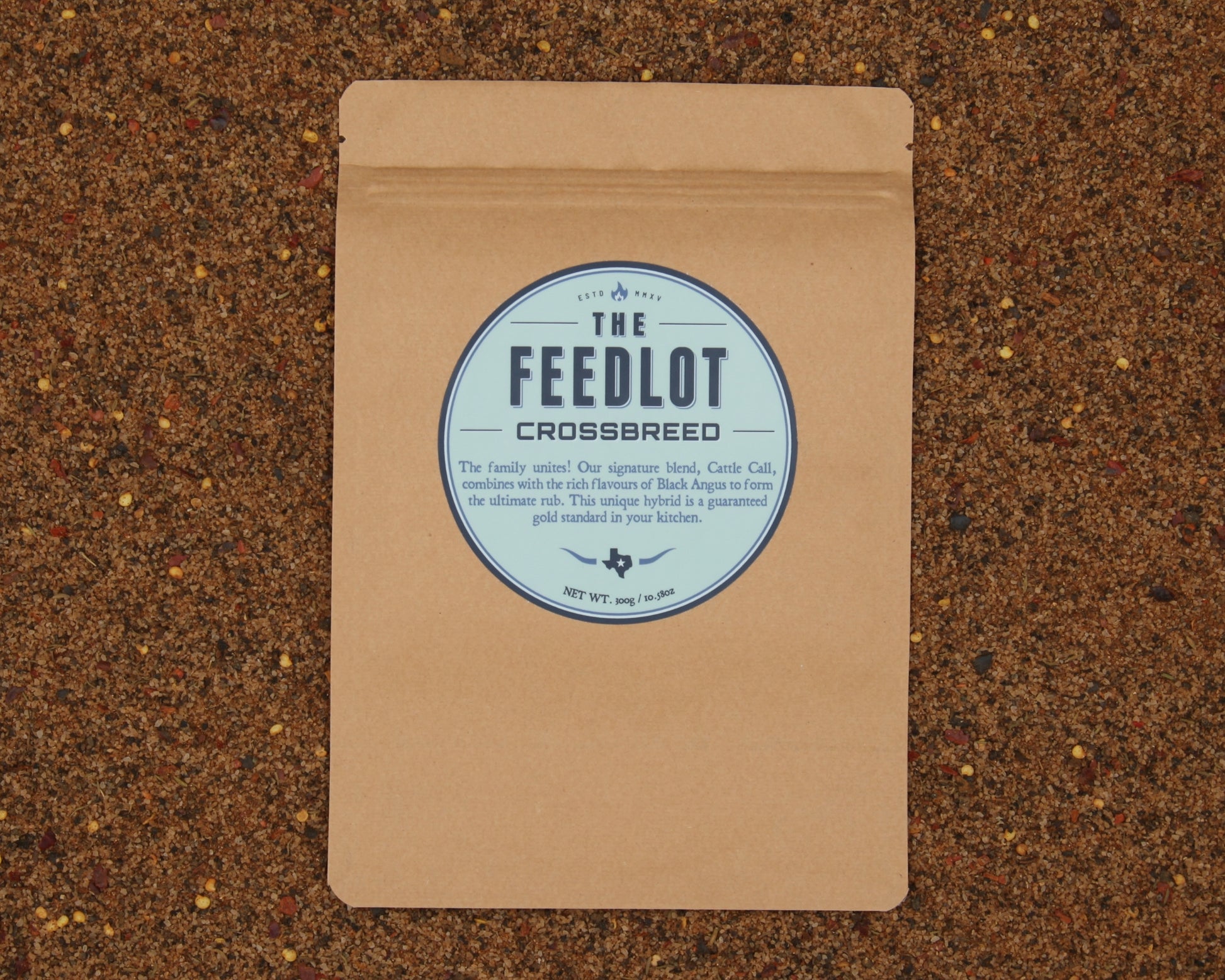 A brown paper package labeled "Crossbreed" by The Feedlot rests on a textured surface with mixed grains. The label touts a hybrid rub combining their signature blend, Carre Cali, with their renowned Black Angus rub. The net weight is 5.9 oz/160g.