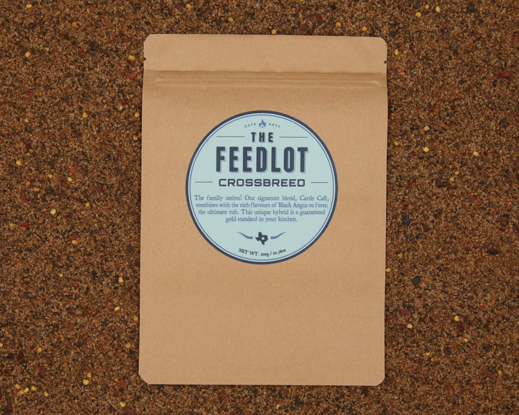 A brown paper package labeled "Crossbreed" by The Feedlot rests on a textured surface with mixed grains. The label touts a hybrid rub combining their signature blend, Carre Cali, with their renowned Black Angus rub. The net weight is 5.9 oz/160g.